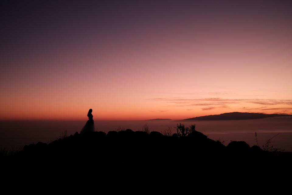 silhouet van een bruid die op een rots staat bij zonsondergang