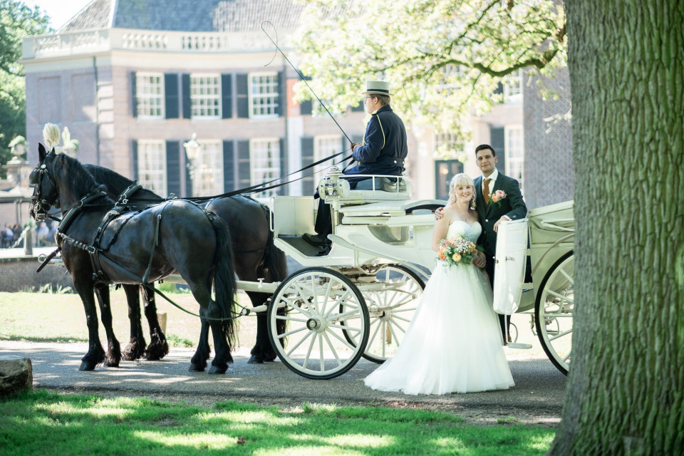 een bruid en bruidegom poseren voor een met paarden getrokken koets