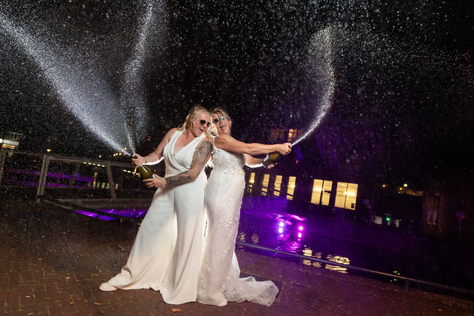 twee bruiden in trouwjurken die champagne spuiten