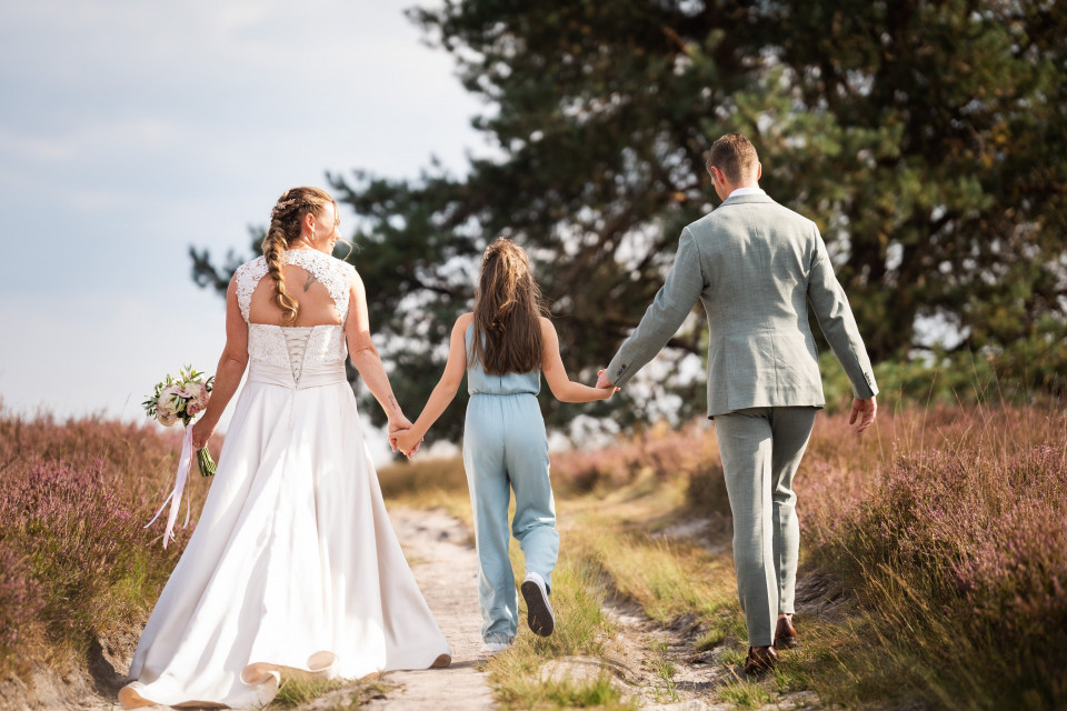 een bruid en bruidegom lopen samen met hun dochter op een zandweg