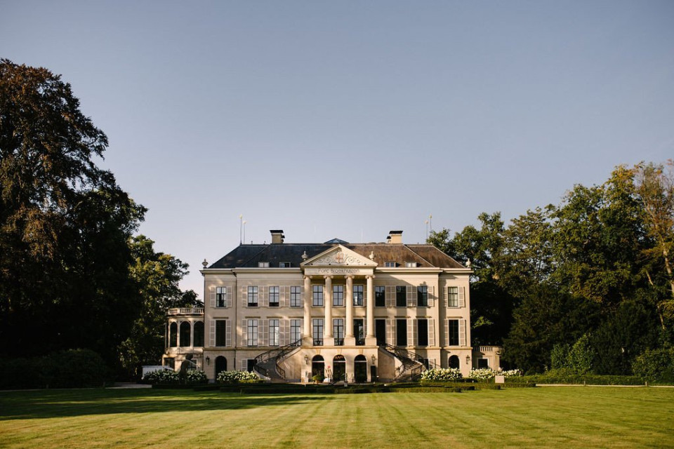een groot landhuis bovenop een weelderig groen veld