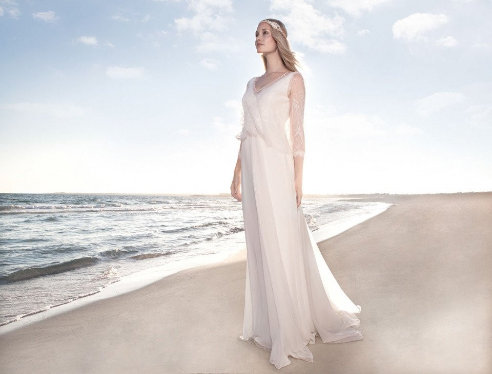 een vrouw in een trouwjurk die op het strand staat