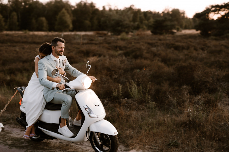 een bruid en bruidegom die op een scooter rijden op het platteland