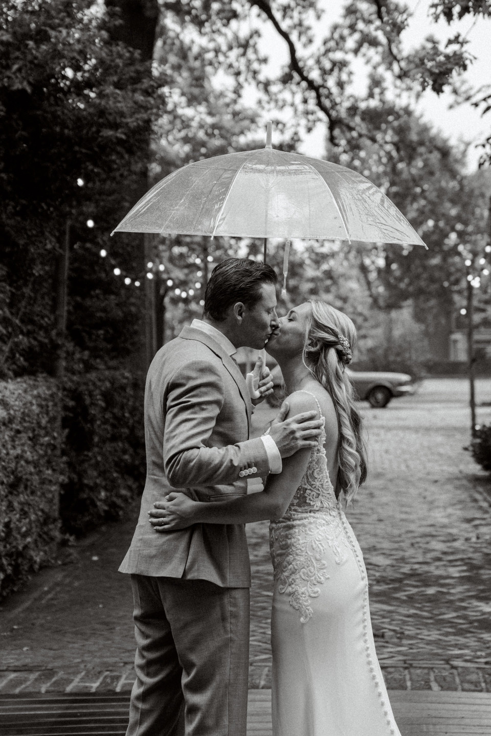 bruid en bruidegom kussen onder een paraplu in de regen
