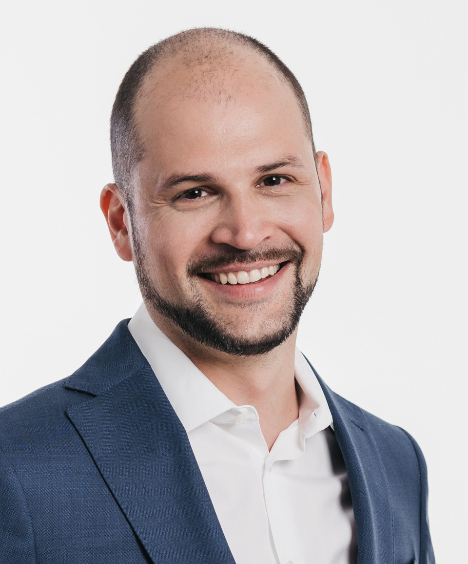 een afbeelding van een man in een pak die glimlacht voor de camera