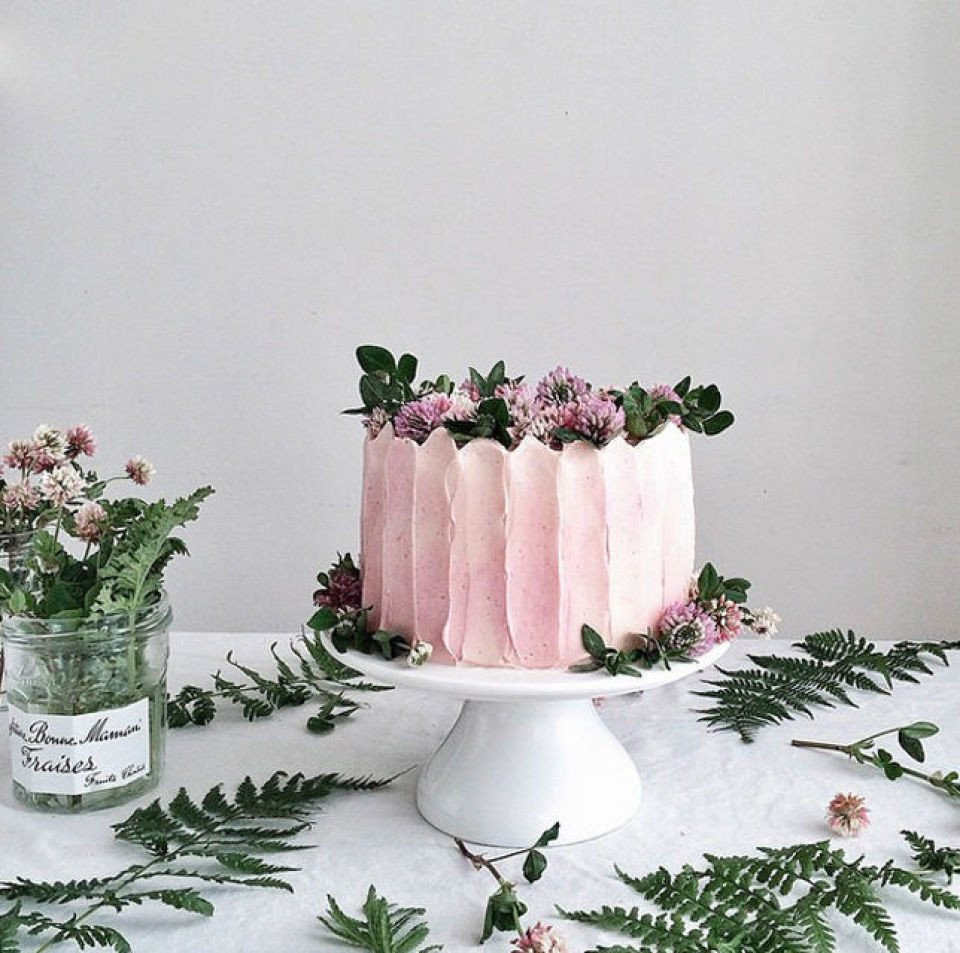 een roze taart met bloemen en groen op een tafel