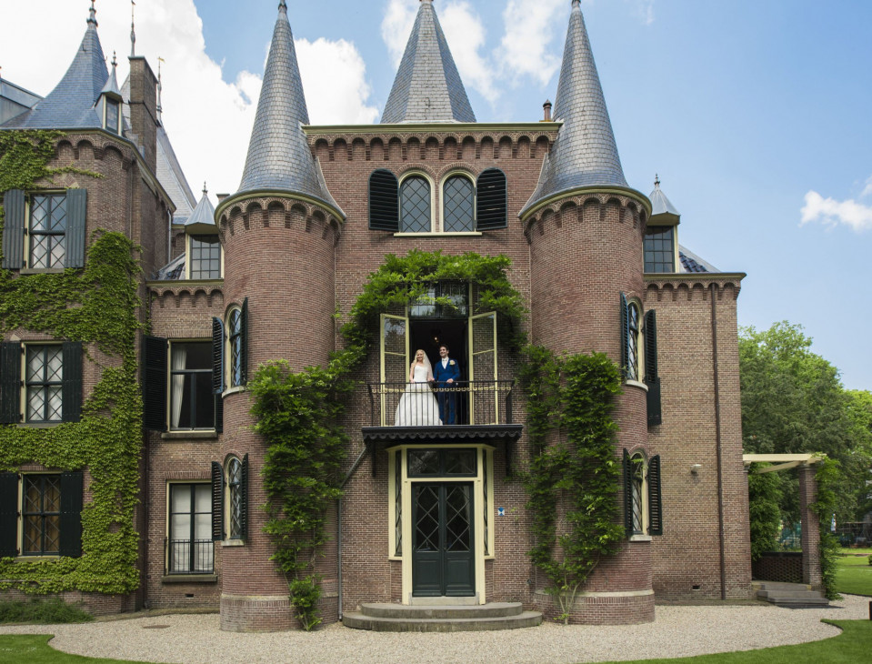 een bruidspaar staat op het balkon van een kasteel