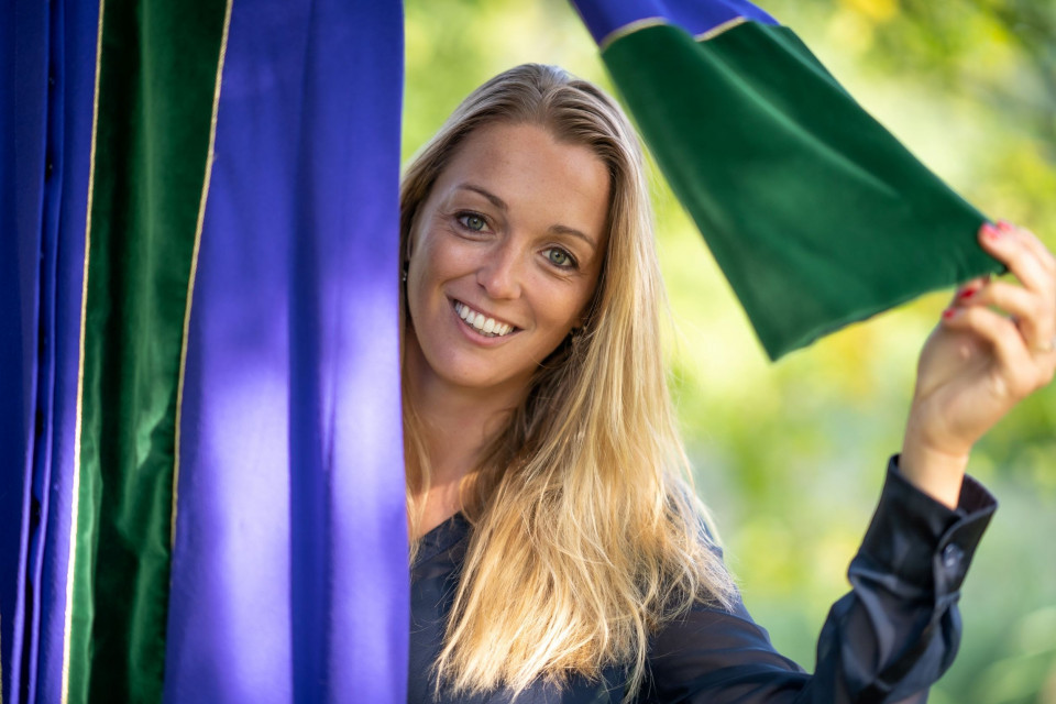 een vrouw glimlacht terwijl ze een groen en blauw gordijn vasthoudt