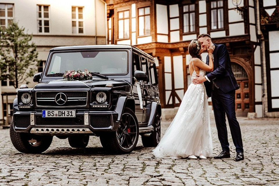 een bruid en bruidegom staan naast een mercedes g-klasse