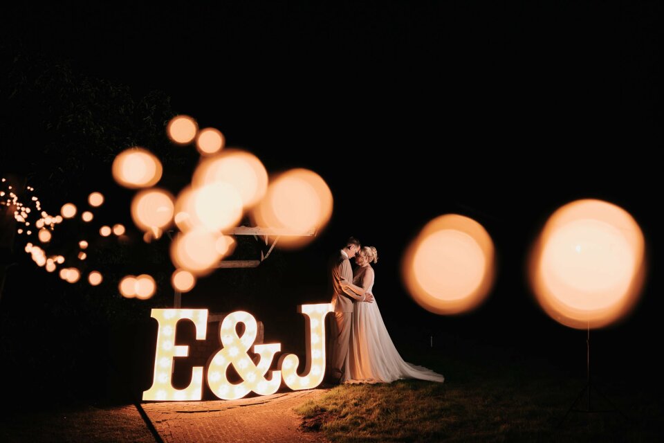 de bruid en bruidegom die voor de oplichtende letters staan