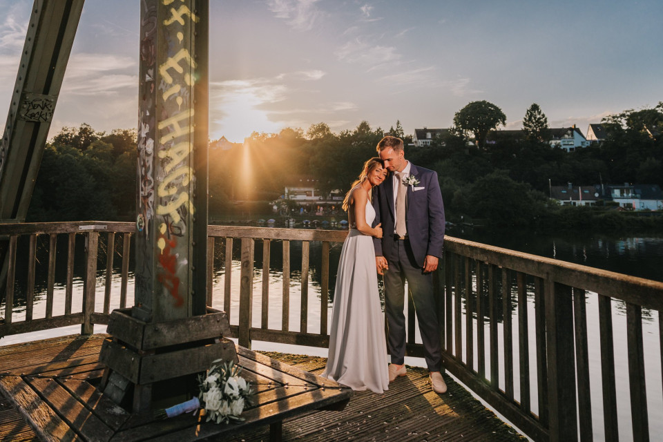 een bruid en bruidegom poseren voor een foto op een brug bij zonsondergang