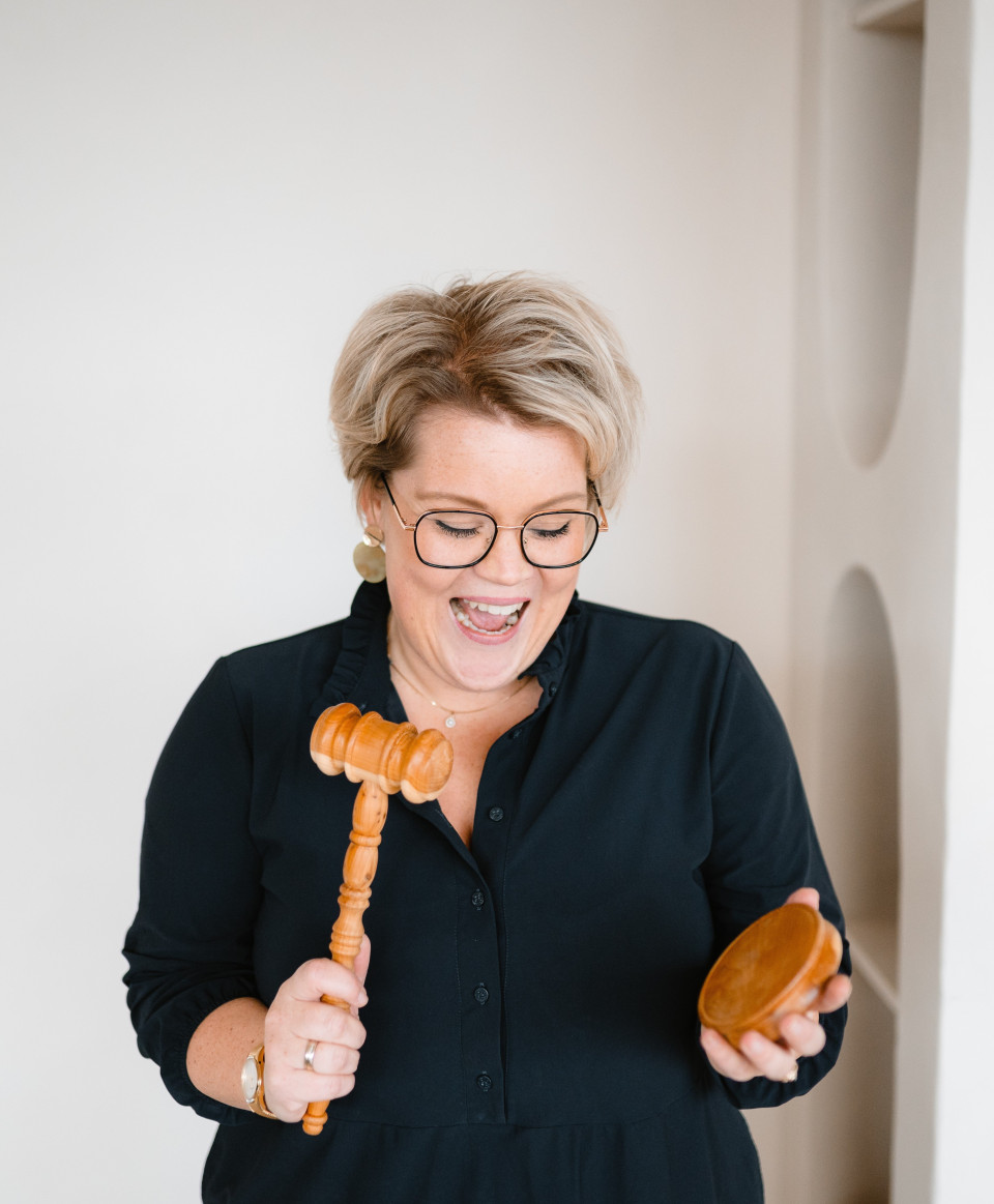 een vrouw met een bril die een houten hamer vasthoudt