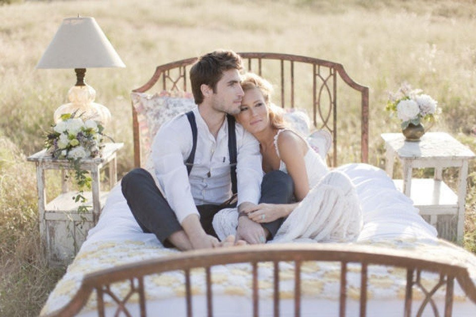 een bruid en bruidegom zitten op een bed in een veld