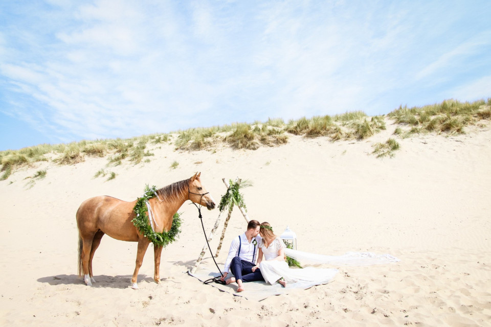 een bruid en bruidegom zitten op het zand met een paard