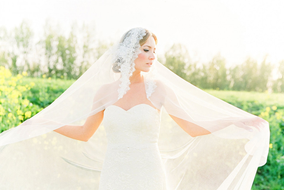 een bruid in een witte jurk en sluier staat in een veld