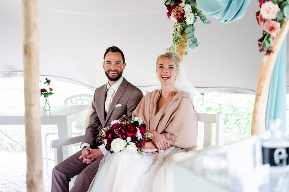 een bruid en bruidegom zitten onder een tent met bloemen