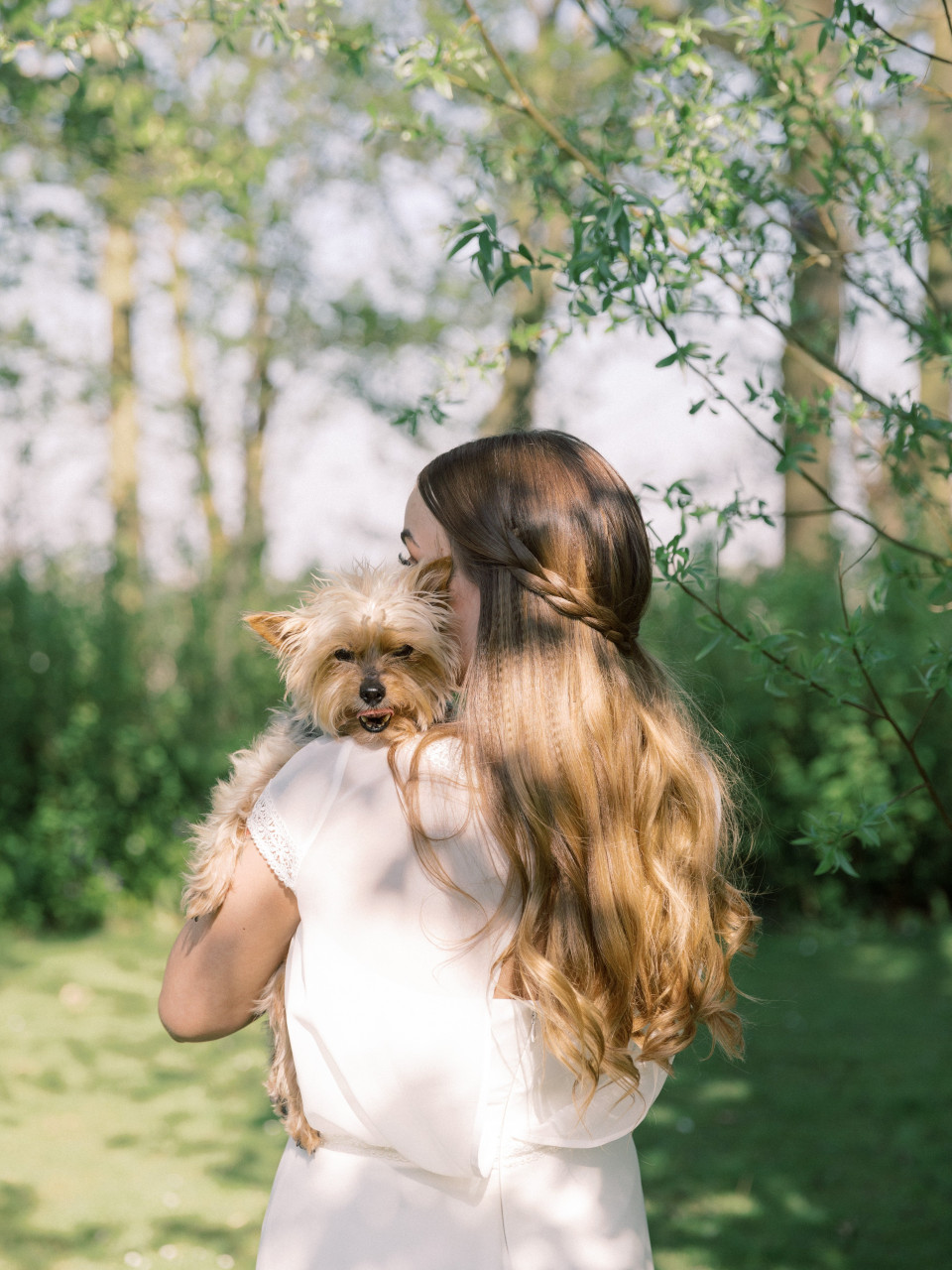 een vrouw in een witte jurk die een kleine hond vasthoudt