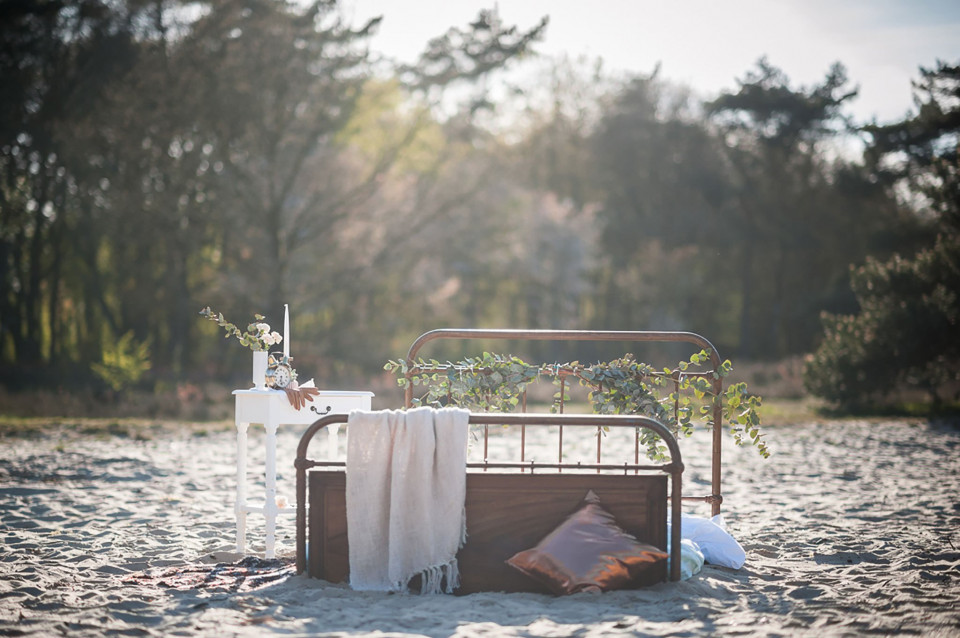 een bed met een wit laken en bloemen op het strand