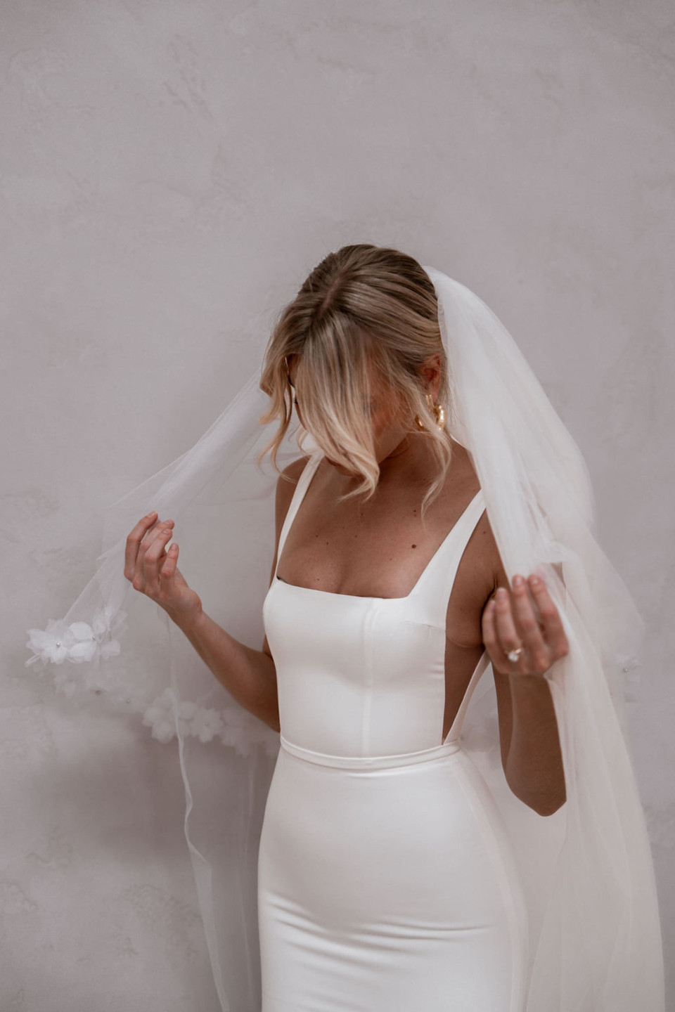 een vrouw in een witte trouwjurk staat voor een muur