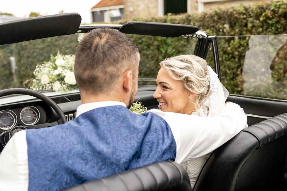 een bruid en bruidegom die op de achterbank van een cabriolet zitten