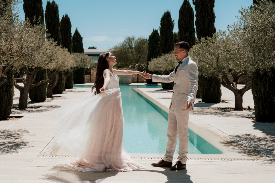 een bruid en bruidegom staan bij een zwembad voor olijfbomen