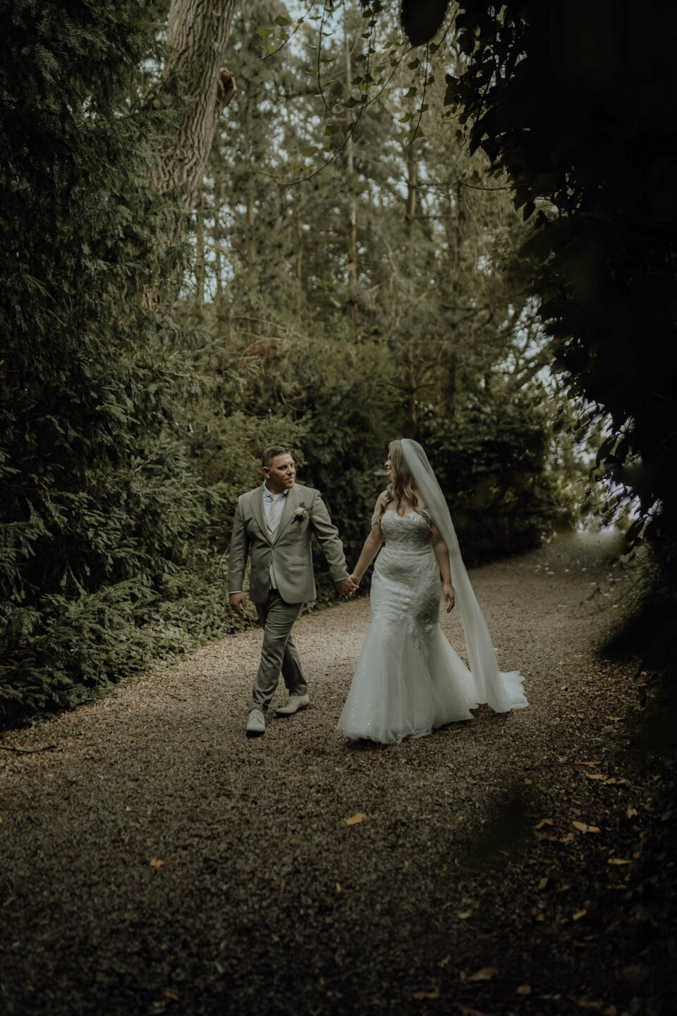 een bruid en bruidegom die over een pad in het bos lopen