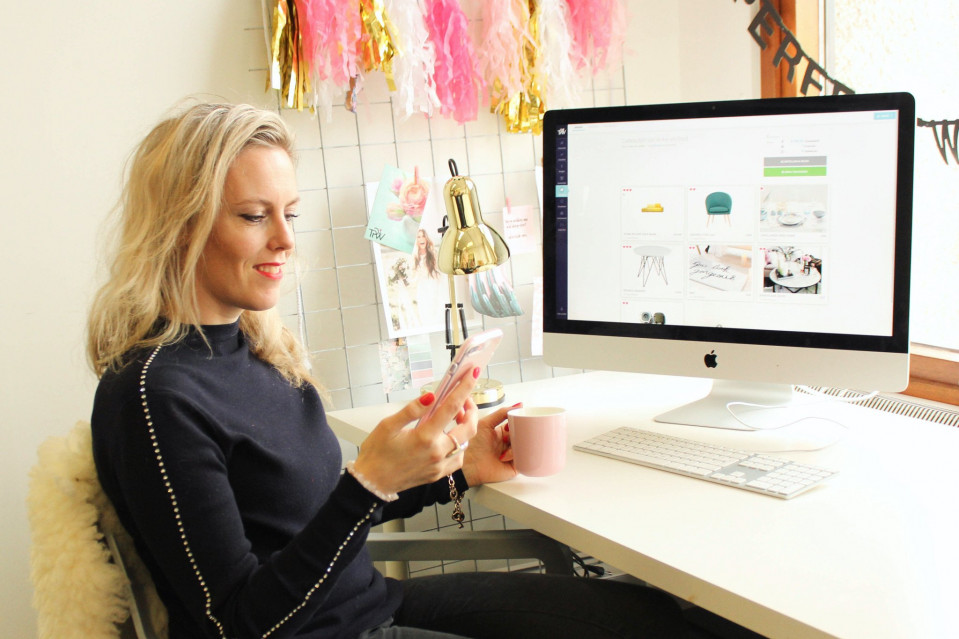 een vrouw zit aan een bureau met een computer en een mobiele telefoon