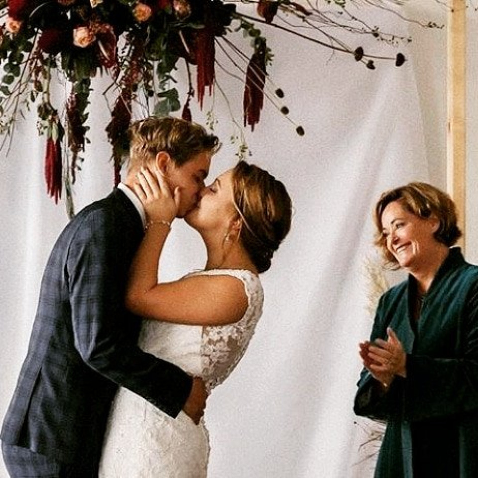 een bruid en bruidegom kussen onder een bloemenboog