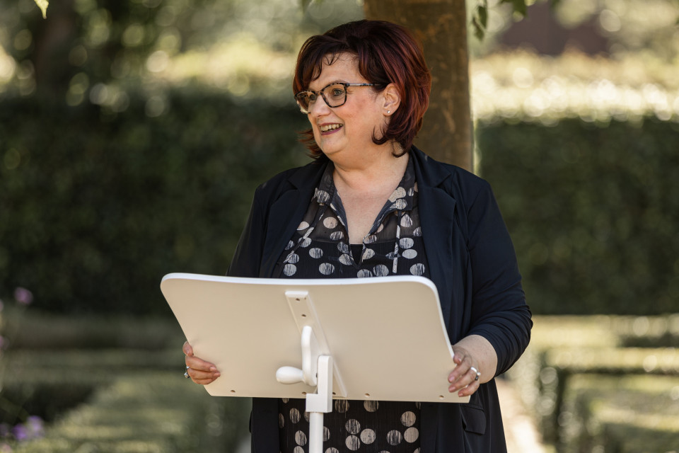 een vrouw met bril en een zwart shirt staat voor een wit bord