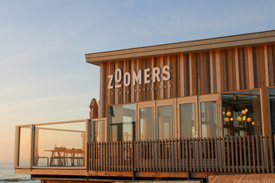 een restaurant op het strand met een bord dat zegt 'zoniers' aan de zijkant van het gebouw en een strand op de achtergrond