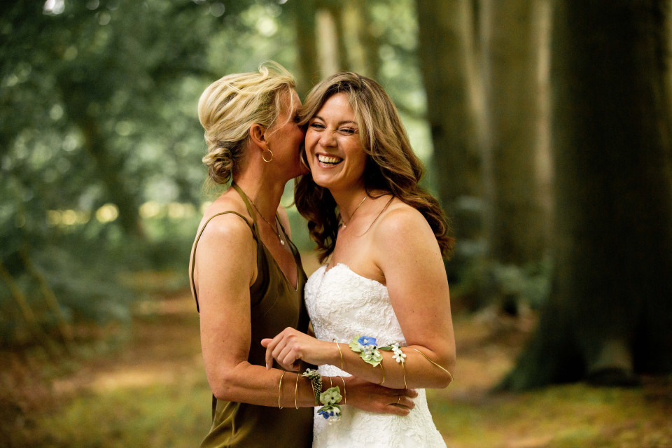 twee vrouwen in trouwjurken knuffelen in het bos