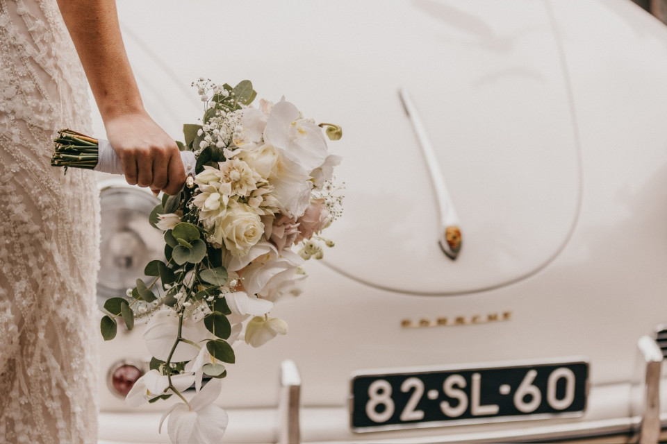 een bruid met een boeket en een vintage auto