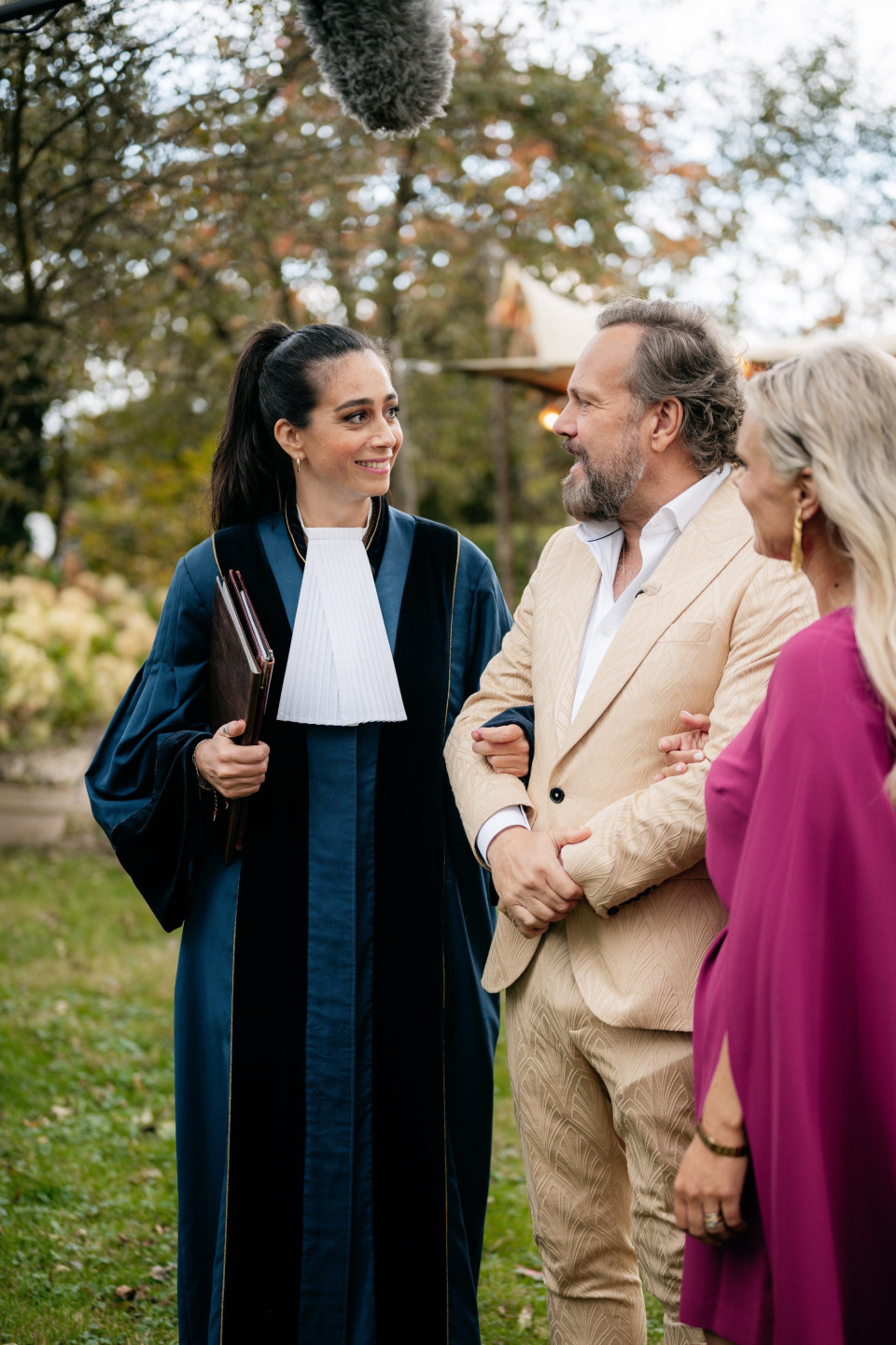 een man in een gewaad die met een vrouw in een paarse jurk praat en een man in een zwart gewaad en een witte shirt