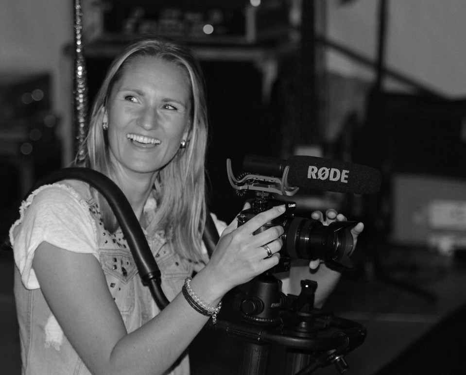 een vrouw die een camera vasthoudt en glimlacht terwijl ze voor een microfoon staat