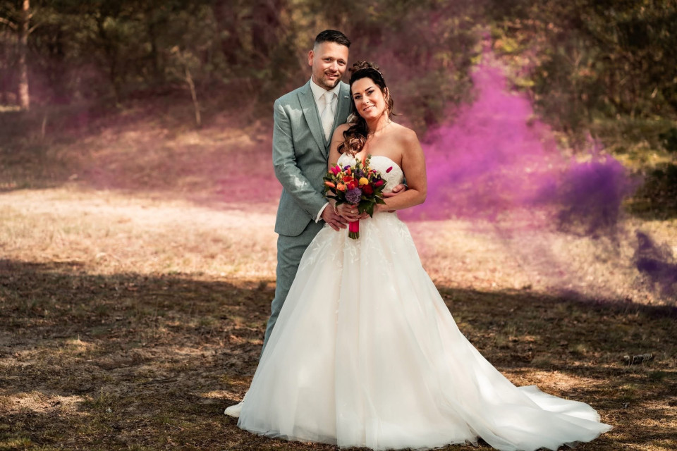 een bruid en bruidegom poseren voor een foto met paarse rook op de achtergrond