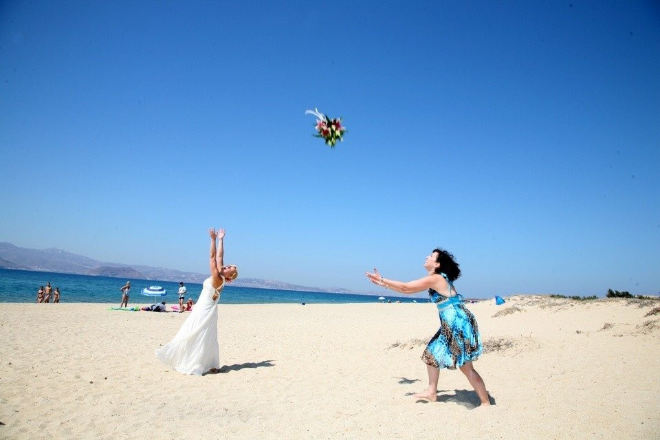 twee bruiden die bloemen naar elkaar gooien op het strand