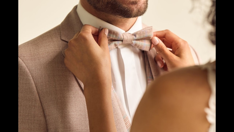 een man past zijn strikje aan terwijl een vrouw naar hem kijkt