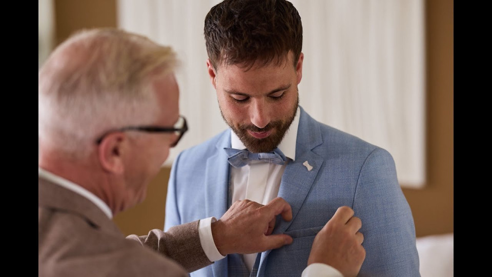 een man past zijn pak aan terwijl een andere man naar hem kijkt
