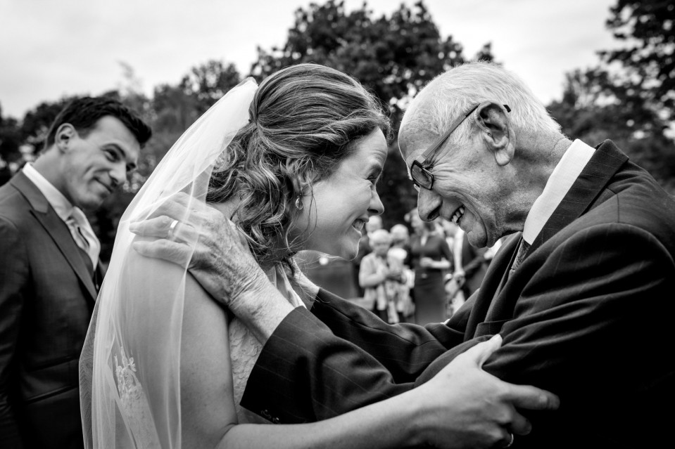 een bruid omhelst haar opa terwijl hij toekijkt
