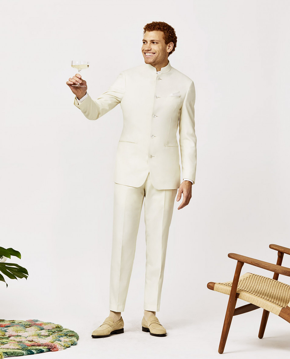 een man in een wit pak en schoenen houdt een wijnglas vast