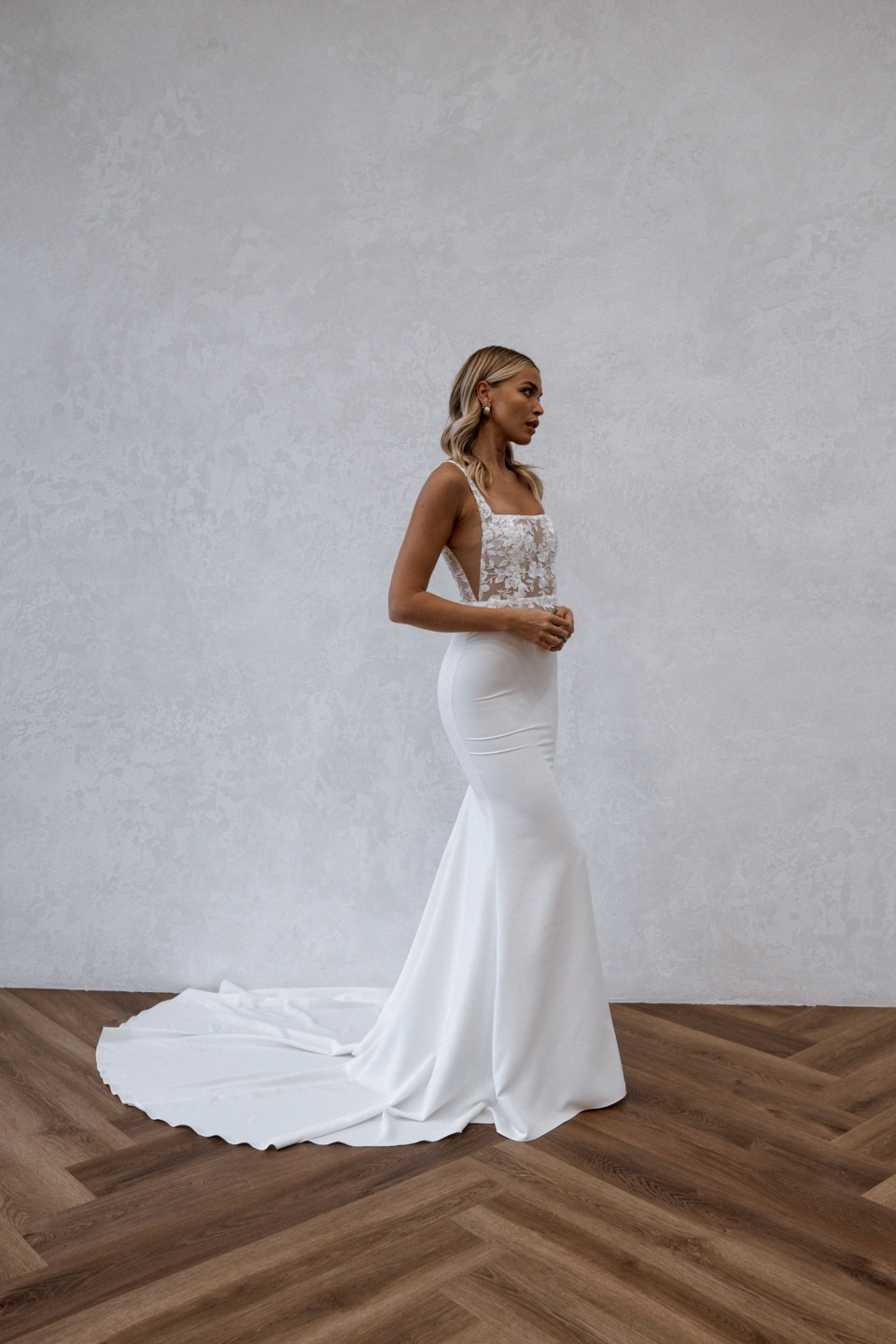 de bruid in een witte trouwjurk staat voor een houten vloer