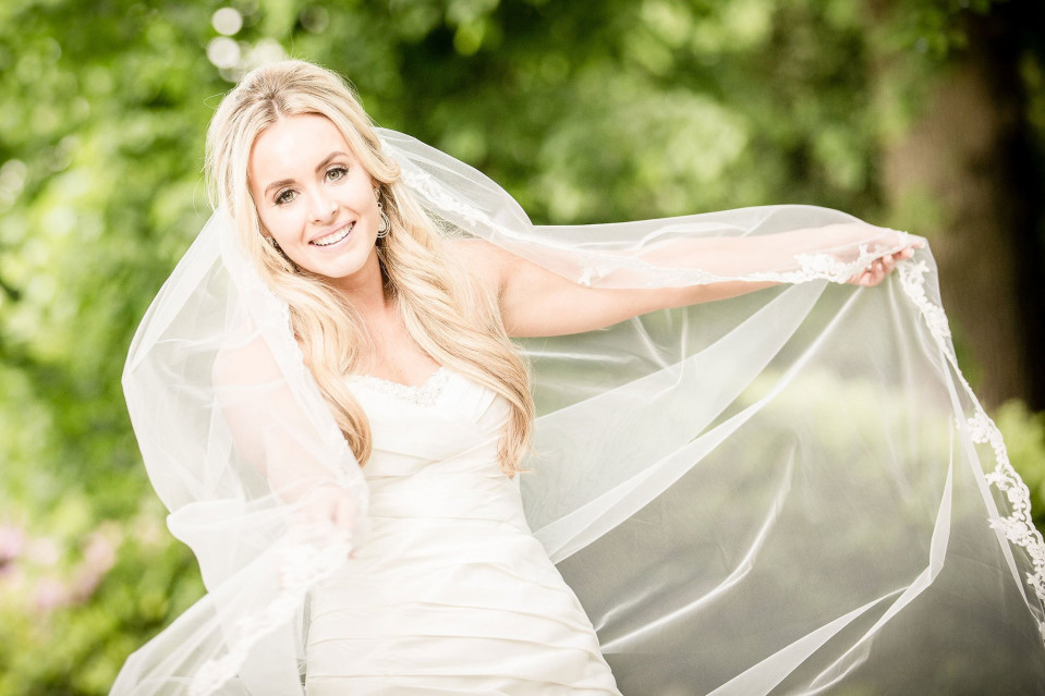 een mooie blonde bruid in een trouwjurk die haar sluier vasthoudt