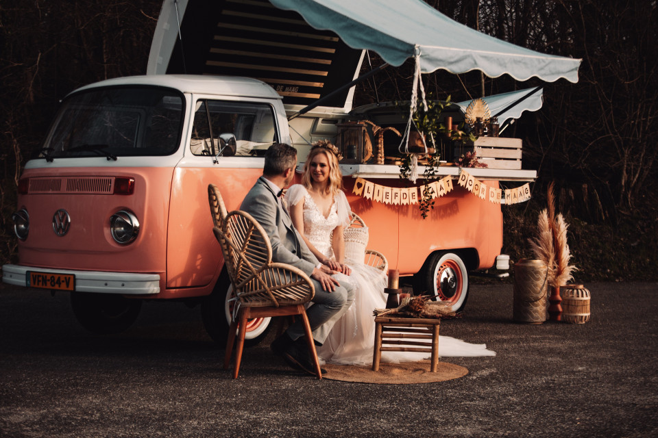 een bruid en bruidegom zitten voor een roze vw-bus