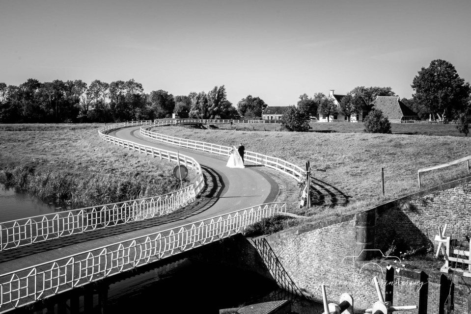 een zwart-wit foto van een bruid en bruidegom die over een brug lopen