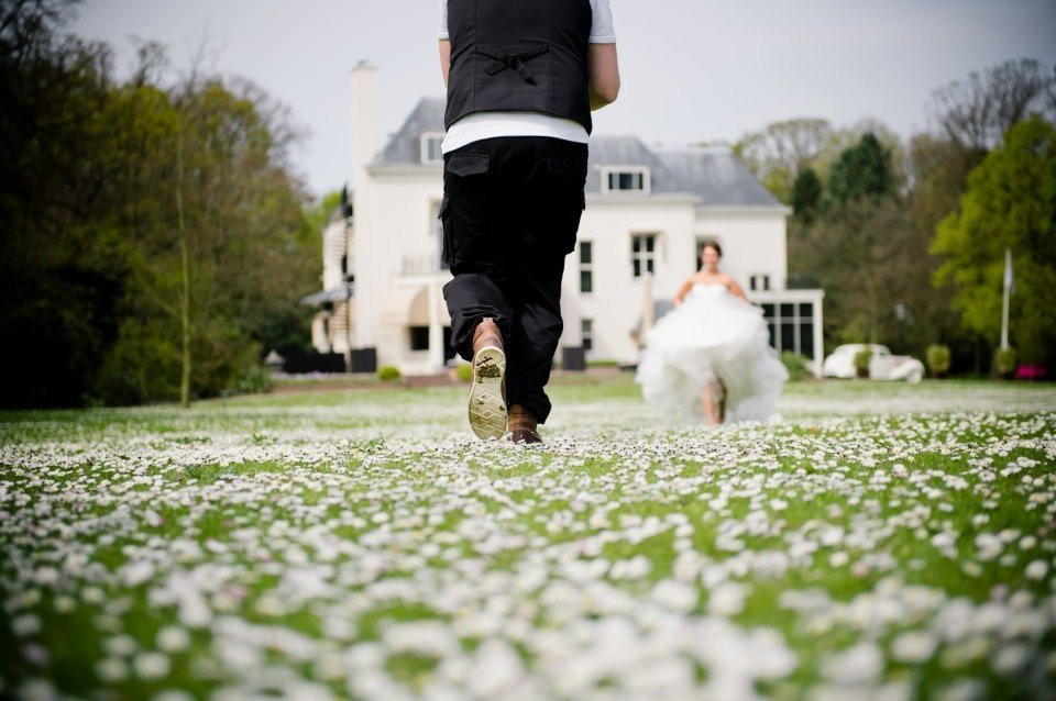 een bruidspaar dat door het gras rent voor een groot huis