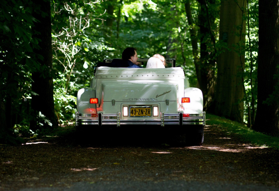 een bruid en bruidegom in een vintage auto op een bospad