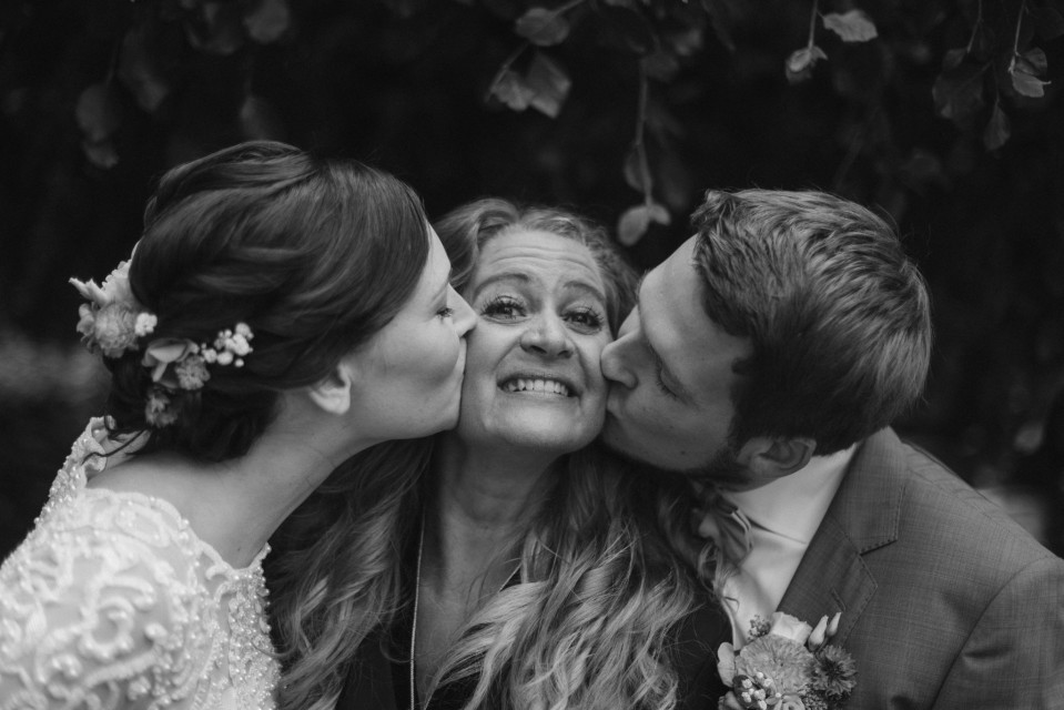 een bruid en bruidegom kussen terwijl hun moeder hen kust