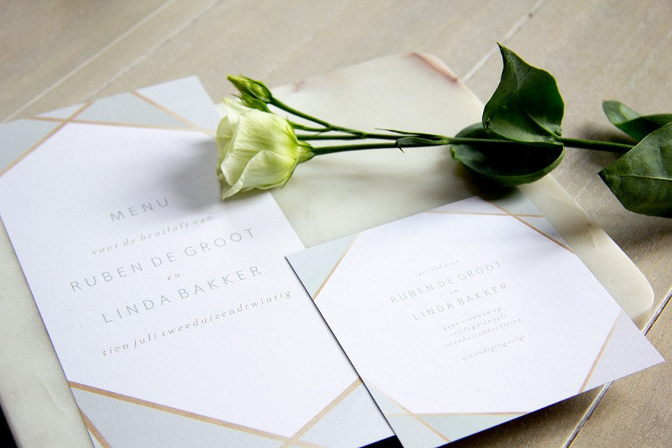 een trouwuitnodiging met een witte roos op een marmeren tafel