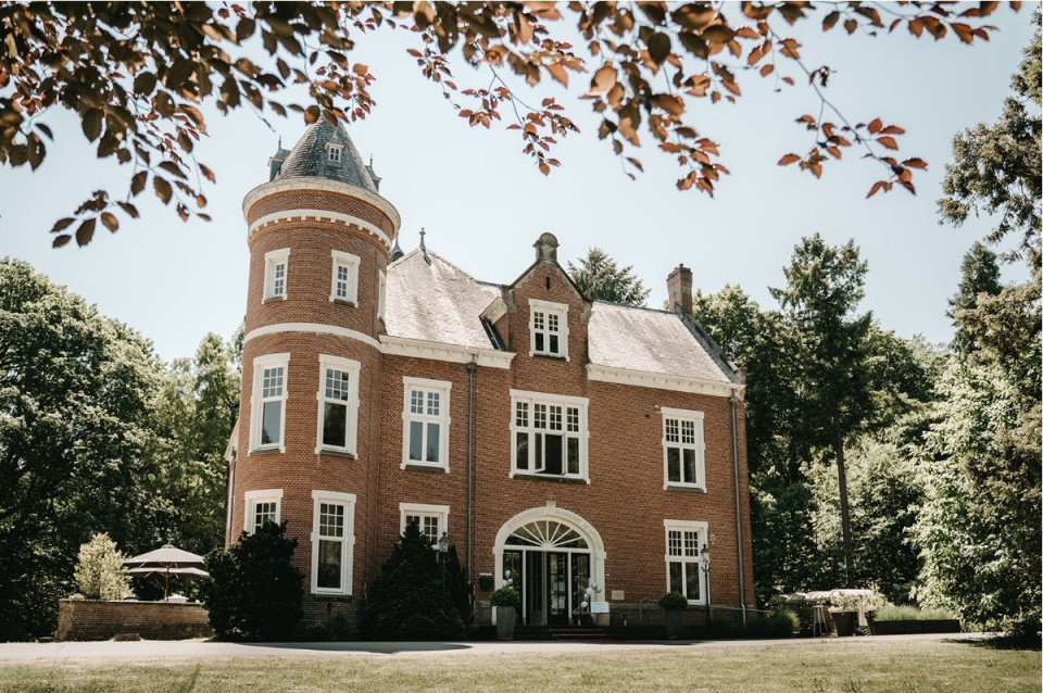 een groot bakstenen herenhuis met een toren en bomen