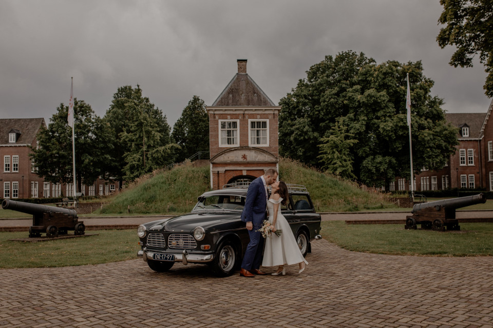 een bruid en bruidegom poseren met hun vintage auto voor het kasteel